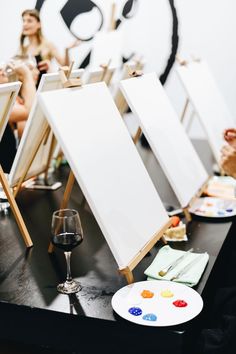 several easels and paintings on a table with people in the background