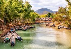 several boats are docked on the water in front of some houses and trees with mountains in the background