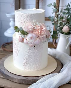 a white wedding cake with pink flowers and greenery on top, sitting on a wooden table