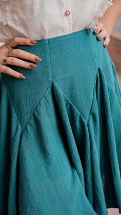 a woman with her hands on her hips wearing a white shirt and teal skirt