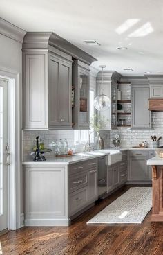 a kitchen filled with lots of gray cabinets and white counter top space next to a wooden floor