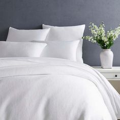 a bed with white sheets and pillows on top of it next to a vase filled with flowers