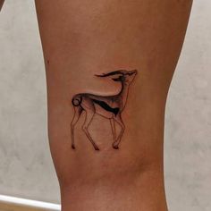 a small deer tattoo on the side of a woman's right leg, it is black and white