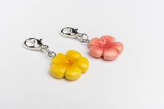 two flower charms are shown on a white surface, one is yellow and the other is pink