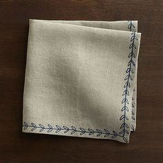 two linen napkins with blue embroidery on them sitting on top of a wooden table