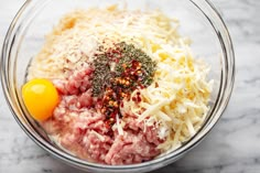 ingredients in a glass bowl for meatloaf on a marble counter top, including eggs and cheese