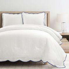 a bed with white sheets and blue trimmings in a room next to a night stand