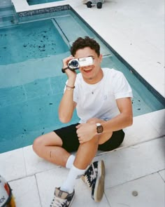 a man sitting next to a swimming pool while holding a camera up to his face