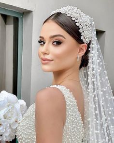 a woman wearing a wedding veil with pearls on the side and flowers in her hair