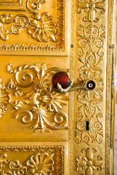 an ornate gold door with a red knob