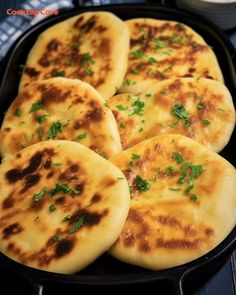 four flat breads in a black pan with parsley on the top and some sauce next to it