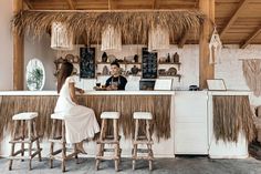 a man and woman sitting at a bar with tiki hut decor on the wall