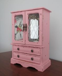 a pink china cabinet with glass doors and drawers on top of a wooden table next to a white wall