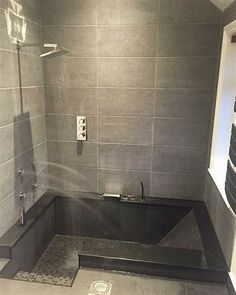 a bathroom with gray tiles and a black bathtub in the corner, next to a shower head