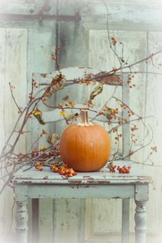 an orange pumpkin sitting on top of a wooden table next to a white wall with branches