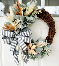 a wreath on the front door with leaves and flowers hanging from it's side