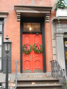 a red door with two wreaths on it's front and stairs leading up to the entrance