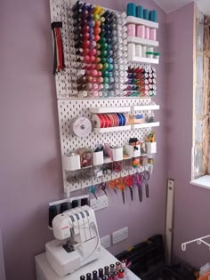 a sewing machine is sitting in front of a wall rack with many different colored thread spools