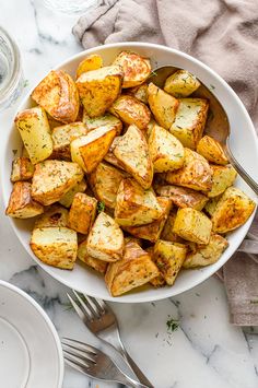 a white bowl filled with cooked potatoes on top of a marble table next to silverware