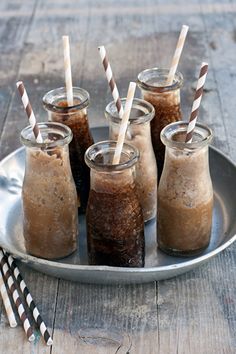 six glasses filled with different kinds of drinks on a plate next to straws and paper straws