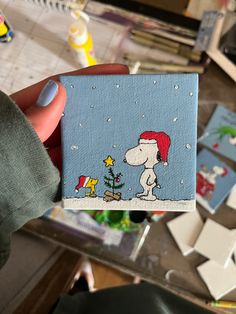 a person holding up a small card with a snoopy christmas scene on it