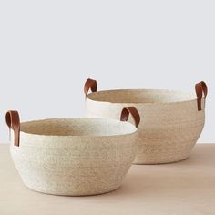 three woven baskets with handles on top of a wooden table, one is white and the other is brown