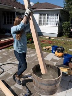 a woman is working on a large wooden cross in front of a house with tools nearby