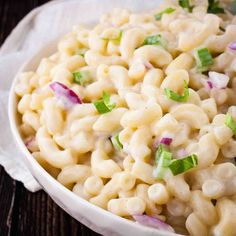 macaroni salad in a white bowl on top of a wooden table with napkins