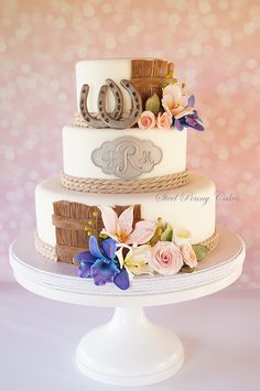 a three tiered cake with flowers and the word love on top is sitting on a white pedestal