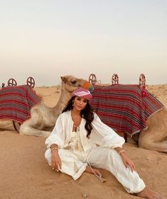 a woman sitting on the ground in front of two camels