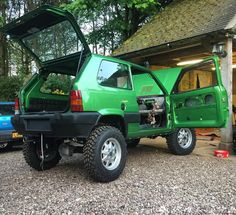 a green pick up truck parked in front of a garage with its doors open and the hood opened