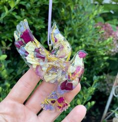 a hand holding a glass bird ornament in it's left hand, with flowers all over it