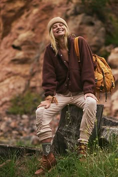 a woman sitting on top of a tree stump with a backpack over her shoulder and smiling