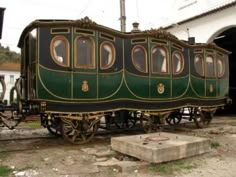 an old green train car sitting in front of a white and black building with windows