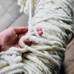 a person holding yarn in their hands on the floor with it's ends twisted up