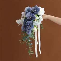 a bridal bouquet with blue and white flowers hanging from it's side, being held by a hand