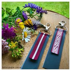 two key chains sitting on top of a piece of wood next to flowers and plants