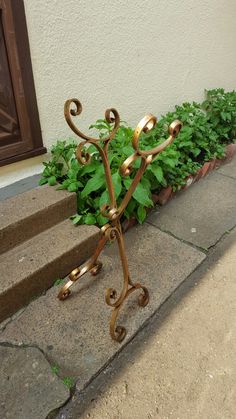 a metal plant stand sitting on the side of a sidewalk next to a potted plant