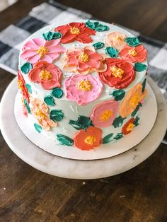 a white cake with flowers on it sitting on top of a wooden table next to a black and white checkered napkin