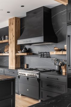 a kitchen with black cabinets and an oven in the center is decorated with wood shelving