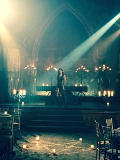 a woman standing on top of a stage in front of candles and chandeliers