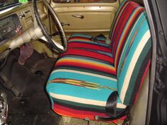 the interior of an old car with multicolored striped seat covers and steering wheel