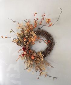 a wreath with dried flowers and branches hanging on the wall next to a white wall