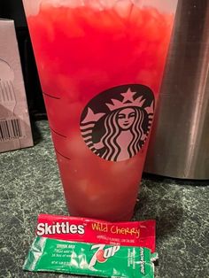 a red drink in a cup next to a bag of skittles