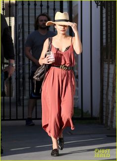 a woman in a dress and hat walks down the street with her hand on her head