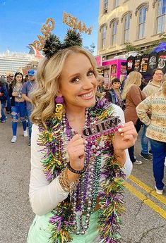 a woman is standing in the middle of a street holding up her cell phone and wearing a mardi gras costume