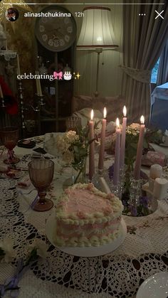 a table topped with a cake covered in frosting and lit candles next to a window