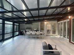 a large open room with white furniture and glass doors on the outside wall, leading to an outdoor dining area