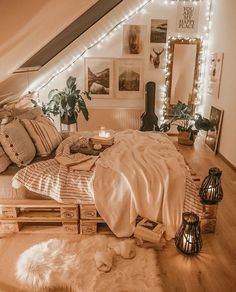 a bed with pillows and blankets in a room decorated with string lights, plants and pictures on the wall