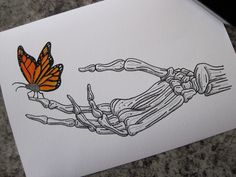 an orange butterfly sitting on top of a piece of paper next to a skeleton hand